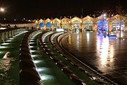 Vue de nuit à travers une place ouverte dominée par une caractéristique de l'eau à long incurvée qui est allumé décorative À l'autre côté de la place il ya la façade cintrée d'un bâtiment de la gare