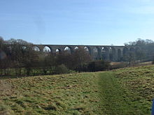 viaduc en pierre avec plusieurs arches, en partie masquée par tress
