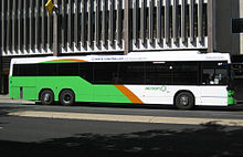 Vert clair, orange et blanc bus se arrêtant en face du bâtiment de plusieurs étages.