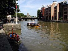 Un taxi jaune sur l'eau entre quais de pierre. La banque a bien grands bâtiments et la distance est un pont à trois arc.