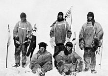 Cinq hommes (trois permanents, deux assis sur le sol glacé) dans les vêtements polaire lourde. Tout l'air épuisé et malheureux. Les hommes debout mènent mâts et un drapeau de l'Union des mouches sur un mât en arrière-plan. Le parti de Scott au Pôle Sud. De gauche à droite: Oates; Bowers; Scott; Wilson; Evans
