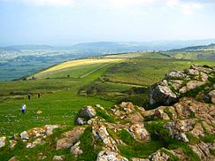 Rochers en face des espaces ouverts herbeuses avec les marcheurs. Hills dans la distance