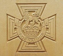 La croix pattée portant la couronne de Saint-Édouard surmontée d'un lion avec l'inscription FOR VALOUR gravé dans la pierre.