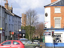 Le coin d'une rue avec une maison publique appelée The Ivy Bush sur le côté droit. Dans le fond, deux tours de briques de grande taille peuvent être considérés plus à gauche.