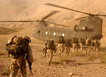 Une ligne de soldats transportant du matériel sur le dos marcher vers un hélicoptère de transport de terrain désertique