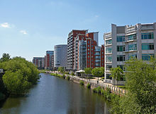 La rivière Aire canalisée découle des Arches sombres sous la gare principale de Leeds vers le bas de l'image. Pour la gauche de la rivière est le verrou qui relie la rivière avec le canal de Leeds et Liverpool. Pour le droit est une rivière à pied sous les immeubles modernes, et au loin, au-delà du viaduc ferroviaire et de la station, sont des bâtiments plus modernes de grande hauteur situés sur le côté ouest du centre-ville.