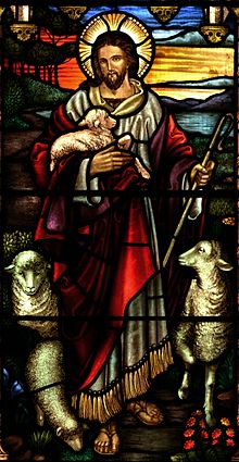 Une représentation de vitraux de Jésus comme un homme de race blanche avec de longs cheveux bruns, une barbe et la croix chrétienne caractéristique inscrit dans le halo derrière sa tête. La figure vêtue d'une couverture blanche robe intérieure par une robe écarlate lâche plus courte. Dépeint comme un Shepard, il tient un cœur dans sa main gauche et portant un agneau dans son droit. Les moutons sont placé à gauche et à droite de la figure.