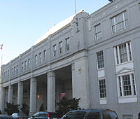 Façade d'un grand bâtiment blanc, la gauche ayant de grands piliers en dessous une bande avec des dizaines de fenêtres et les bonnes histoires de trois grandes fenêtres.