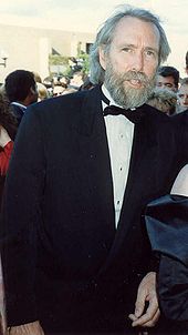 Un homme grand et mince dans ses début des années cinquante, avec des cheveux gris et salée une barbe et vêtu d'un smoking.