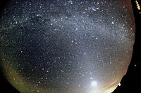 Un météore frappe en bas à gauche, tandis que les arcs de la Voie Lactée généraux et une aube comme des lignes de lumière de l'horizon inférieur. L'image a été prise à travers une lentille incurvée.