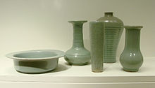 Cinq morceaux de poterie vert pâle. De gauche à droite, un bol cylindrique avec une jante large, plat, un vase avec une longue tige mince et un corps court, presque sphérique, un grand verre mince, un vase large avec pas de tige et une petite ouverture à la top, et un vase avec une longue, mais grande tige et un corps presque sphérique.