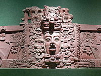 Section de frise en stuc avec un visage humain de premier plan dans le centre, entouré de décoration élaborée.