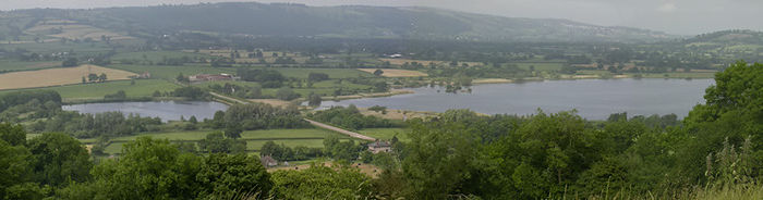 photographie du lac montrant un franchissement routier par une chaussée au Herriots Bridge. Il est entouré de végétation verte avec des collines dans la distance