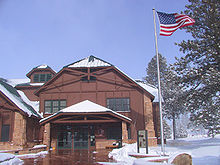 Deux étages du bâtiment en bois à côté de mât de drapeau avec le drapeau américain flottant au vent. Neige au sol.