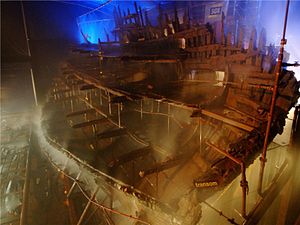 Une section diagonale d'un bateau en bois vu de l'arrière dans un bâtiment d'un air morose allumé alors qu'il est pulvérisé avec de l'eau à partir d'un système d'arrosage
