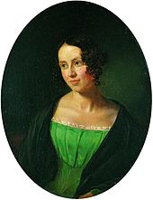 Portrait d'une jeune femme, sur un fond noir. Elle est vêtue d'une robe verte, sur un manteau noir. Elle est à la recherche vers la gauche, un peu sourire.