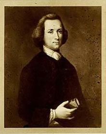 Demi-longueur portrait d'un homme tenant un petit livre dans sa main droite. Il est vêtu d'une veste noire sombre et une chemise blanche.