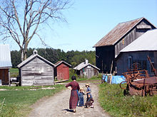 Une femme et ses trois enfants Amish, sur la voie d'une maison et six bâtiments de ferme en bois, passé du matériel agricole.