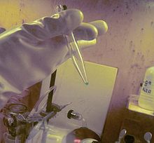 Un très petit échantillon d'un liquide bleu dans une pipette en plastique tenu par une main de porter un équipement de protection lourde