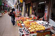 Un client femme parcourant un magasin de fruits. Banane et raisins sont affichés sur le front.