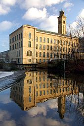 Une usine de pierre se dresse contre un ciel bleu vif, son reflet en miroir dans les eaux ci-dessous.
