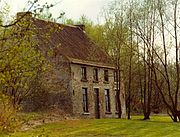 photo d'une maison de brique à deux étages sur la gauche partiellement masquée par les arbres avec une pelouse et d'une rangée d'arbres sur la droite