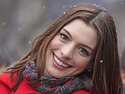 Un headshot d'une jeune femme regardant vers la caméra et souriant. Elle est vêtue d'une veste rouge et foulard et la neige tombe en arrière-plan et l'atterrissage dans ses cheveux.