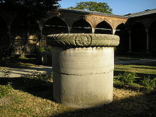 Una columna cilíndrica stout en un patio en frente de arcos palaciegas de estilo islámico