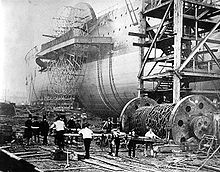 Una vieja fotografía que muestra un gran barco de rueda de paletas de hierro que se puso en marcha hacia los lados, con los obreros empujando grandes baulks de madera bajo un gran tambor de cadenas de hierro